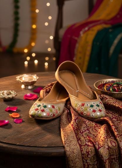 Ujaala beige jutti with embroidered geometric pattern in red, green, and white, featuring mirror work.