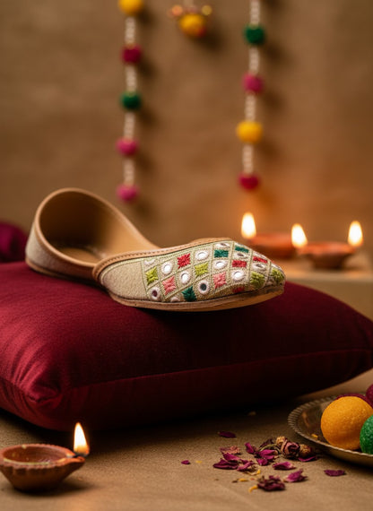 Ujaala beige jutti with embroidered diamond pattern in red, green, and white, featuring mirror work.