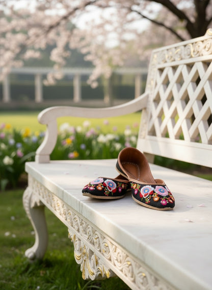 Ujaala Rangrez black jutti with vibrant floral embroidery and bead detailing, resting on a marble bench outdoors.