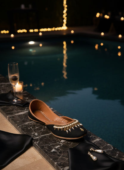 Ujaala Shehnoor black jutti with pearl and gold embellishments, featuring a pointed toe and comfortable flat sole.