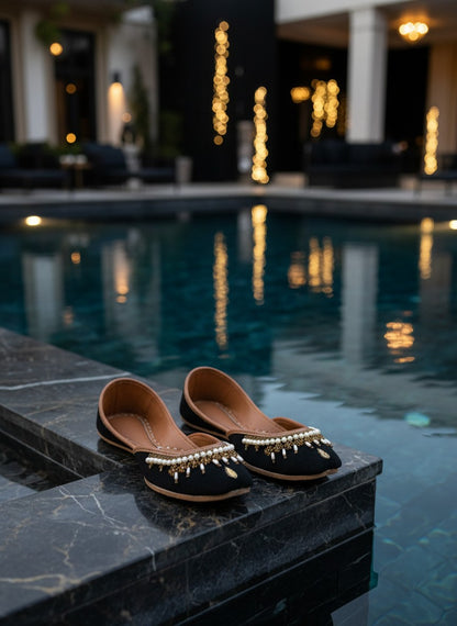 Ujaala Shehnoor black jutti with pearl and gold embellishments, featuring a pointed toe and comfortable flat sole.