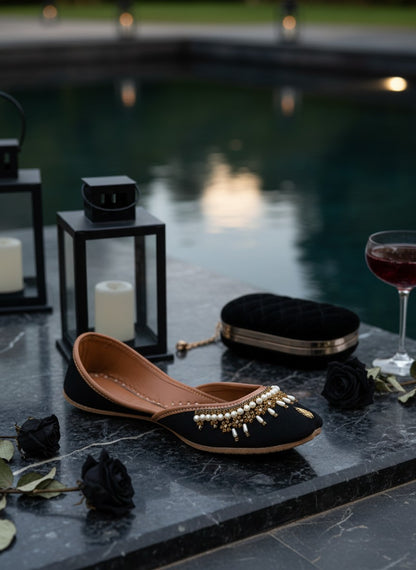 Ujaala Shehnoor black jutti with pearl and gold embellishments, featuring a pointed toe and comfortable flat sole.
