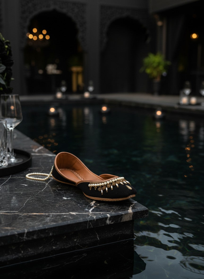 Ujaala Shehnoor black jutti with pearl and gold embellishments, featuring a pointed toe and comfortable flat sole.