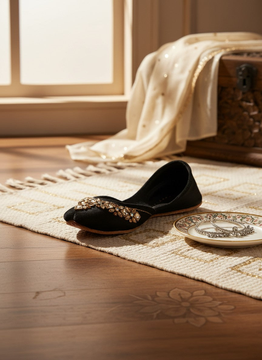 Ujaala black velvet jutti adorned with intricate mirror diamond work and gold embroidery.
