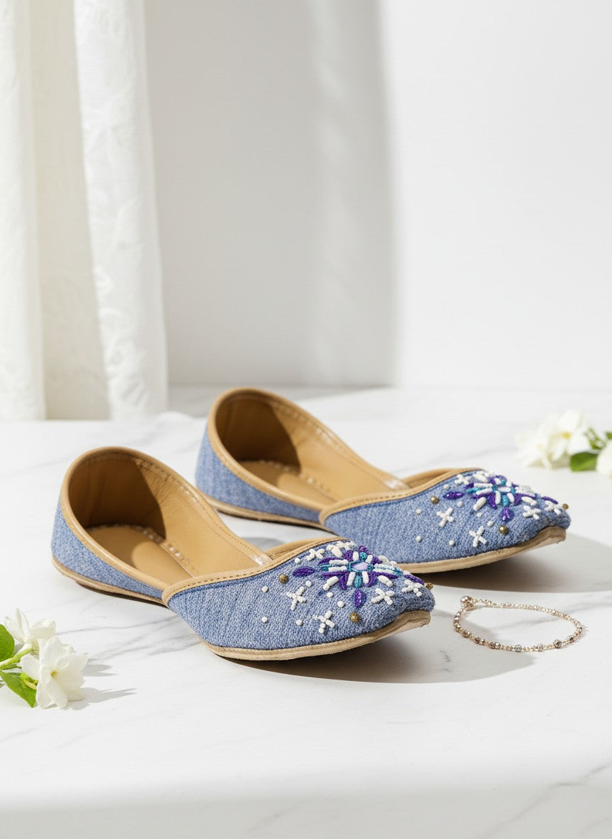 Ujaala Sathi blue denim-textured jutti with white, violet, and blue hand embroidery and bead details.