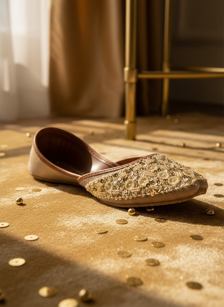 Ujaala gold jutti adorned with sparkling circular discs and beads. Elegant flat shoes with a beige suede finish.
