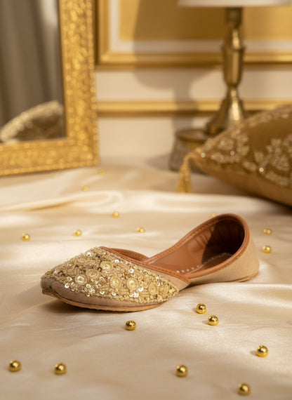 Ujaala gold jutti adorned with sparkling circular discs and beads. Elegant flat shoes with a beige suede finish.
