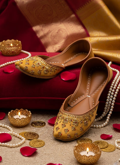 Ujaala Mehwar golden velvet jutti with intricate hand embroidery and red stone detailing. Perfect for festive occasions.