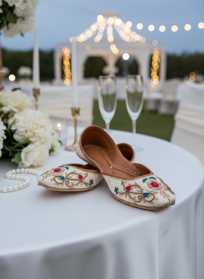 Ujaala Gulkaar ivory jutti with floral embroidery, vibrant threadwork, and mirror accents. Handcrafted festive footwear.